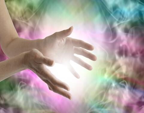 Des mains entourant une lumière dans une composition rose, verte et bleue